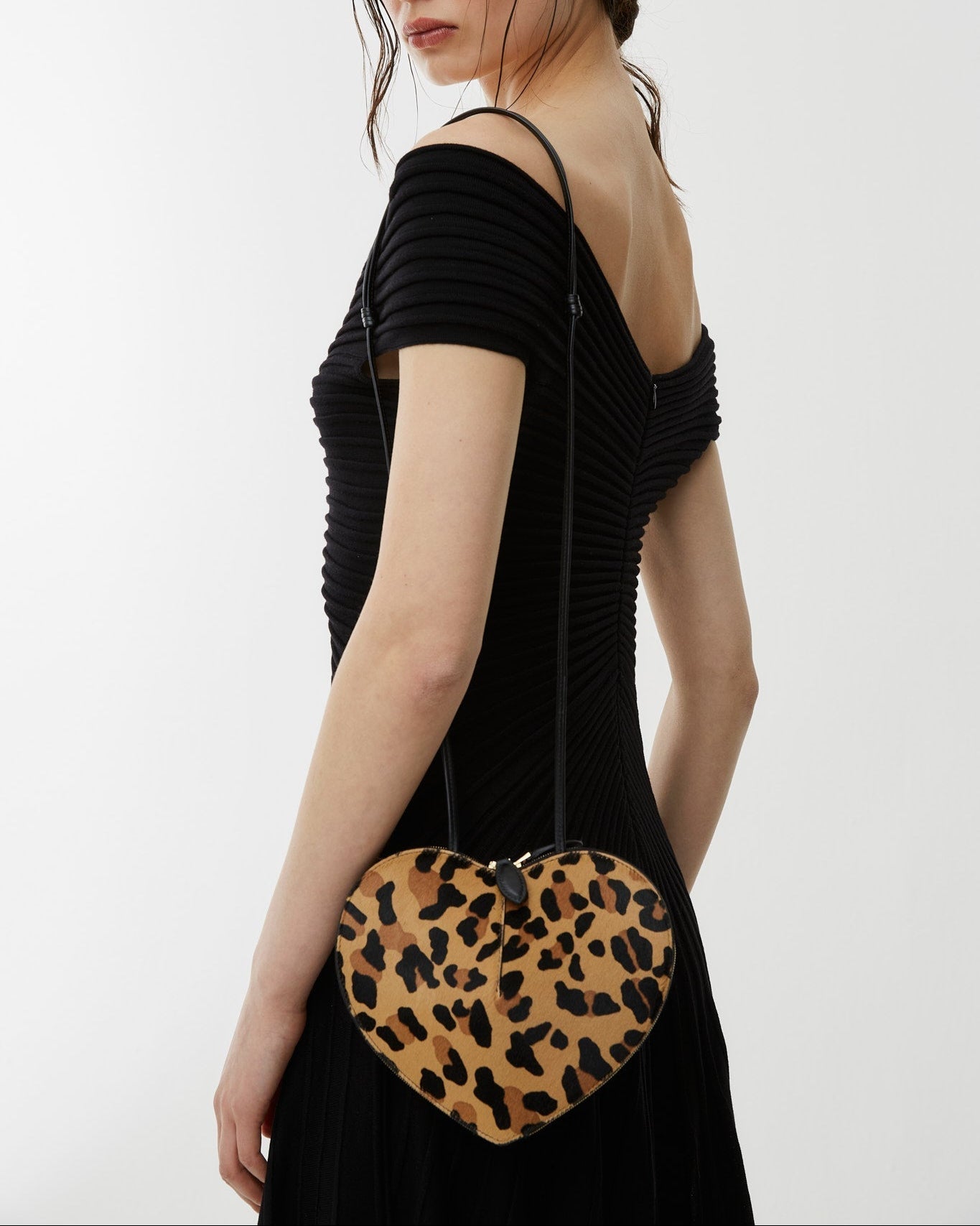 Woman holding a heart-shaped clutch with leopard print design on a white background