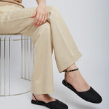 Person wearing beige pants and black shoes sitting on a wire stool against a white background