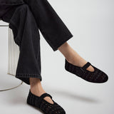 Person wearing black flats and black pants sitting on a white background