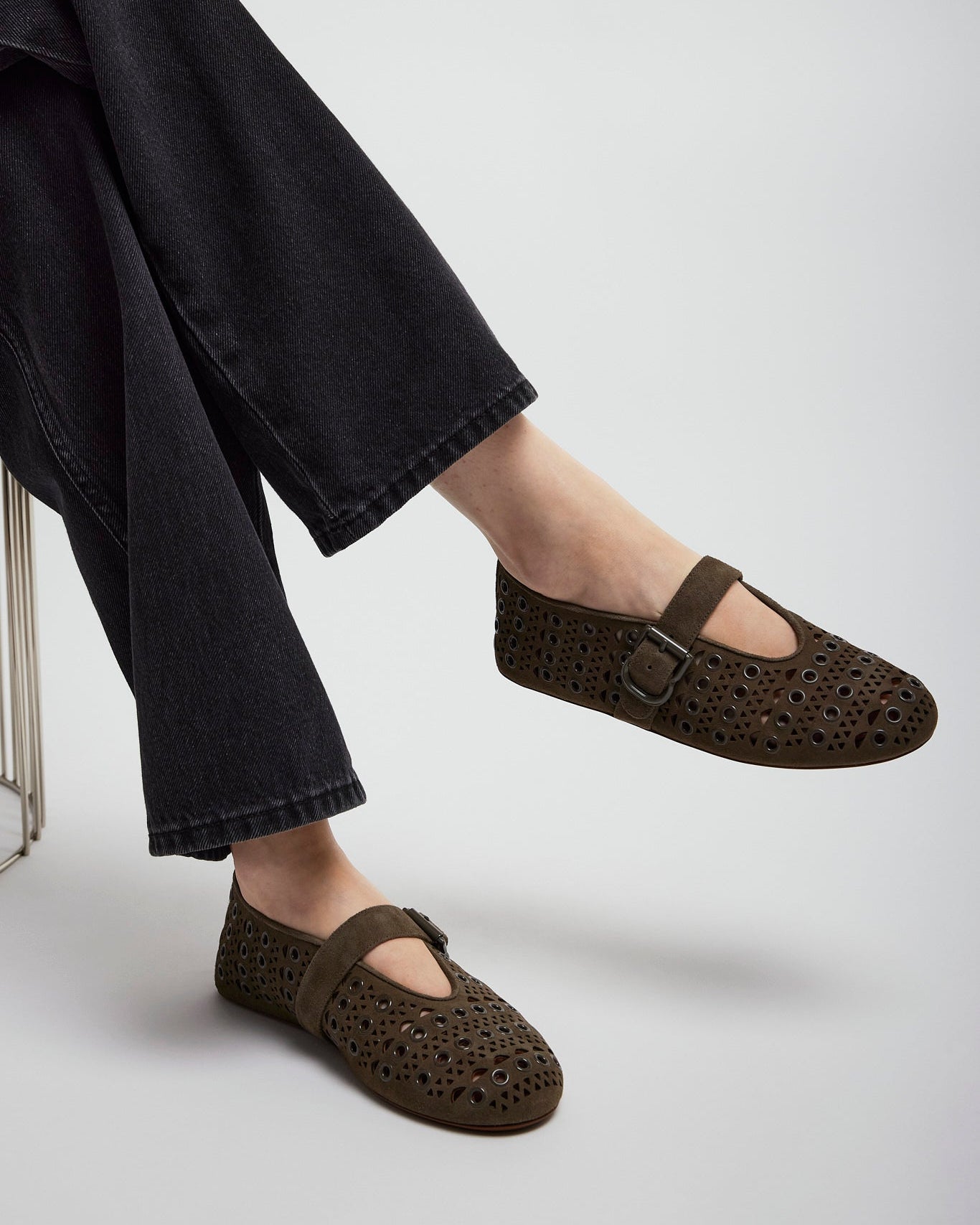 Brown perforated shoes worn with black pants on a light gray background