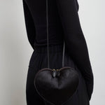 Person wearing a black heart-shaped bag on a plain background