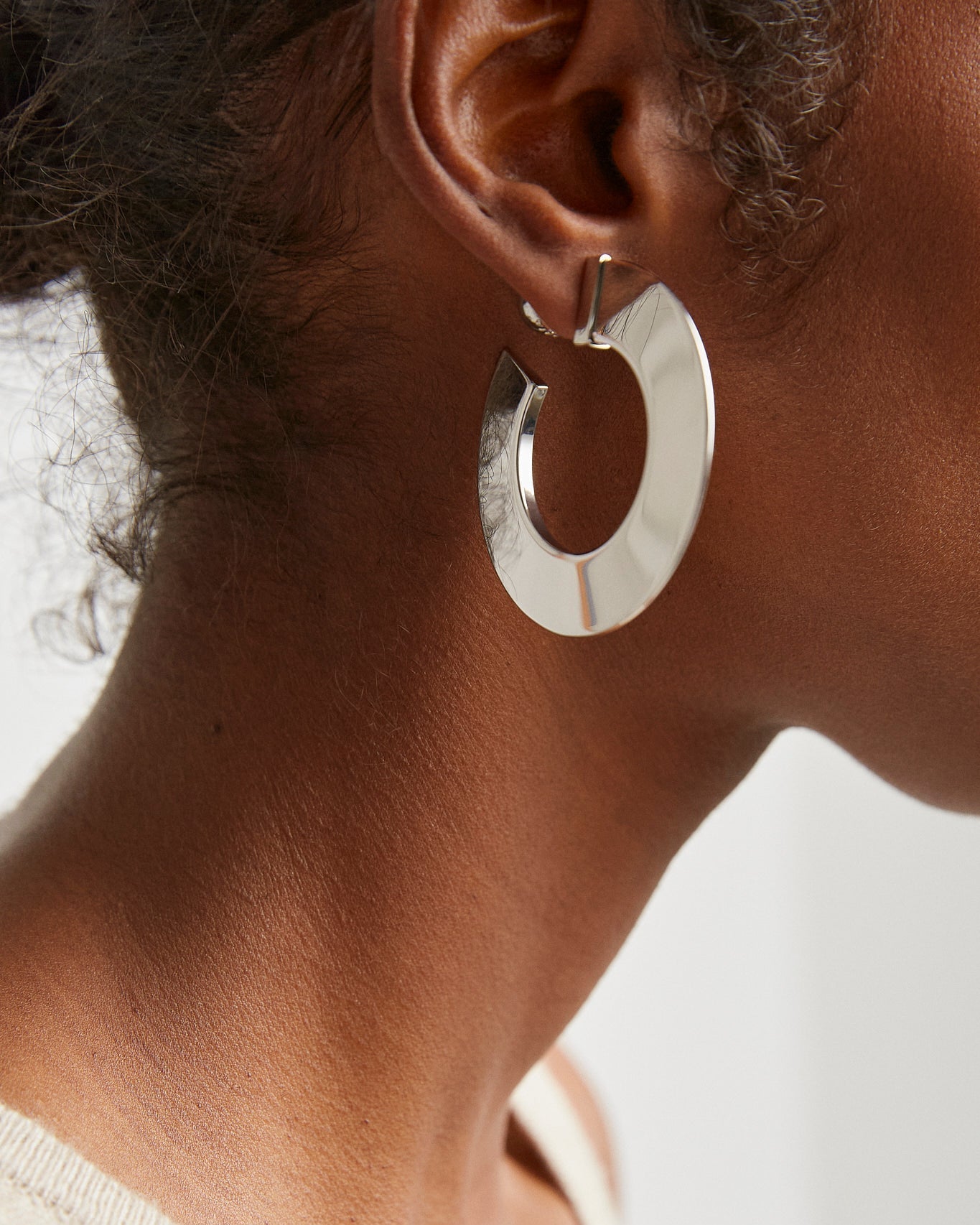 Silver hoop earring worn by a person with a neutral background