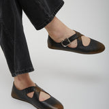 Black leather sandals worn with black pants on a light gray background