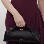 Person holding a black handbag with 'Alaia' branding against a plain background