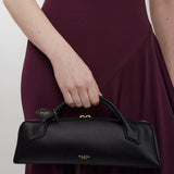 Person holding a black handbag with 'Alaia' branding against a plain background