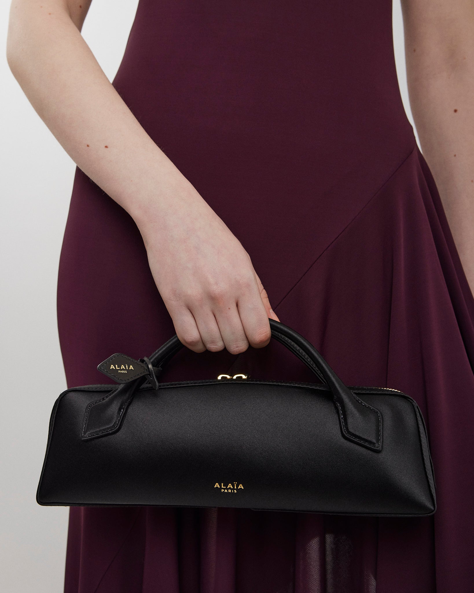 Person holding a black handbag with 'Alaia' branding against a plain background