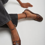 Brown leather shoes worn by a person sitting on a white floor.