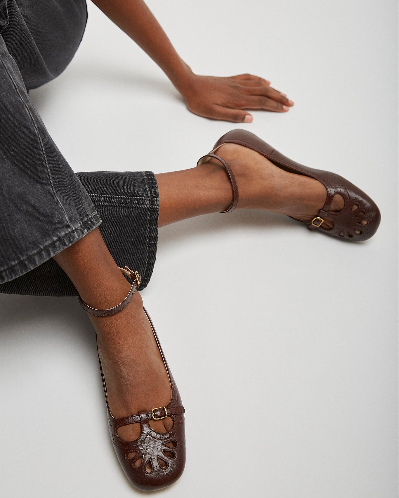 Brown leather shoes worn by a person sitting on a white floor.