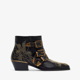 Black ankle boot with gold buckles and studs on a white background