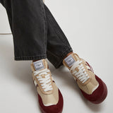 Beige and burgundy sneakers worn with black jeans on a white background