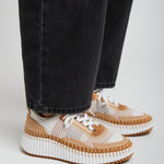 Person wearing black jeans and white sneakers with brown soles on a light gray background