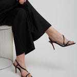 Person wearing black high-heeled sandals with a red sole on a light gray background