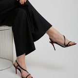 Person wearing black high-heeled sandals with a red sole on a light gray background