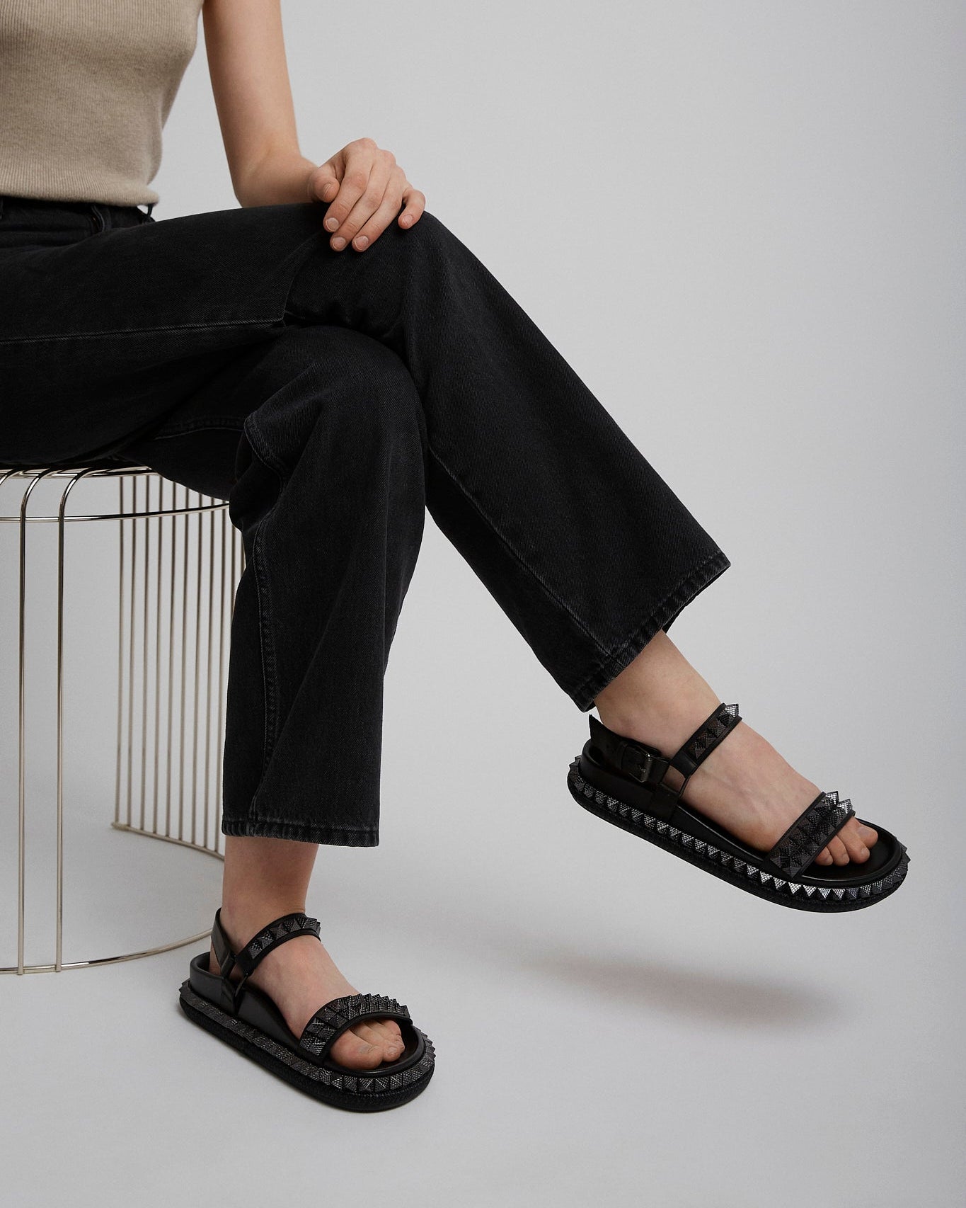 Person wearing black sandals sitting on a white stool against a plain background