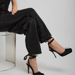 Person wearing black high-heeled shoes sitting on a chair with a plain background
