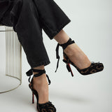 Person wearing black high-heeled shoes with ankle straps on a light gray background