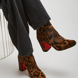 Leopard print boots with red soles worn by a person sitting on a white surface.