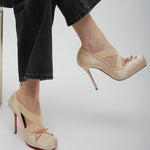 Beige high-heeled shoes worn with black pants on a light gray background