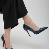 Navy high-heeled shoes with red soles worn by a person in black pants on a light gray background