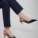 Black high-heeled shoes worn with blue jeans on a light gray background