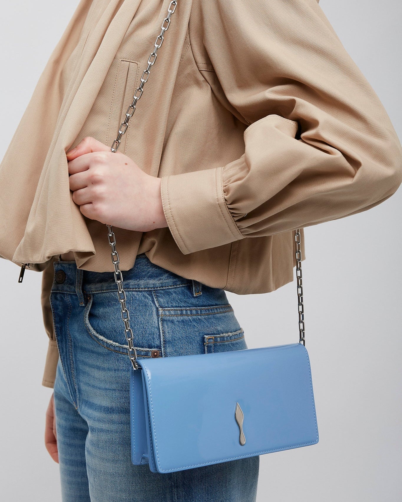 Person wearing a beige jacket and blue jeans with a blue handbag on a plain background