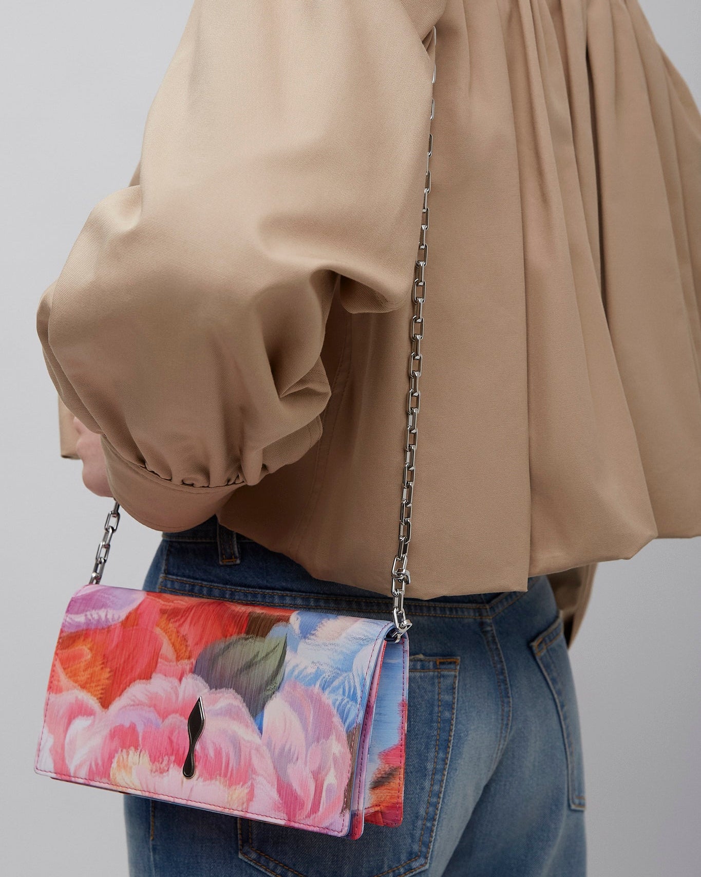 Person wearing a beige jacket with a colorful floral handbag on a plain background