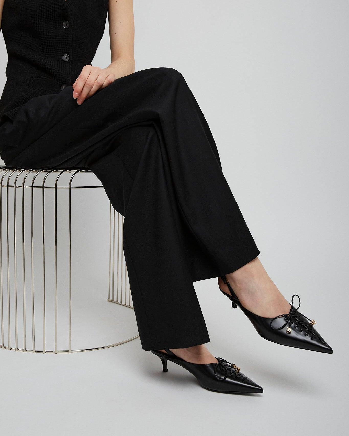 Person wearing a black outfit with high-waisted pants and black shoes on a white background