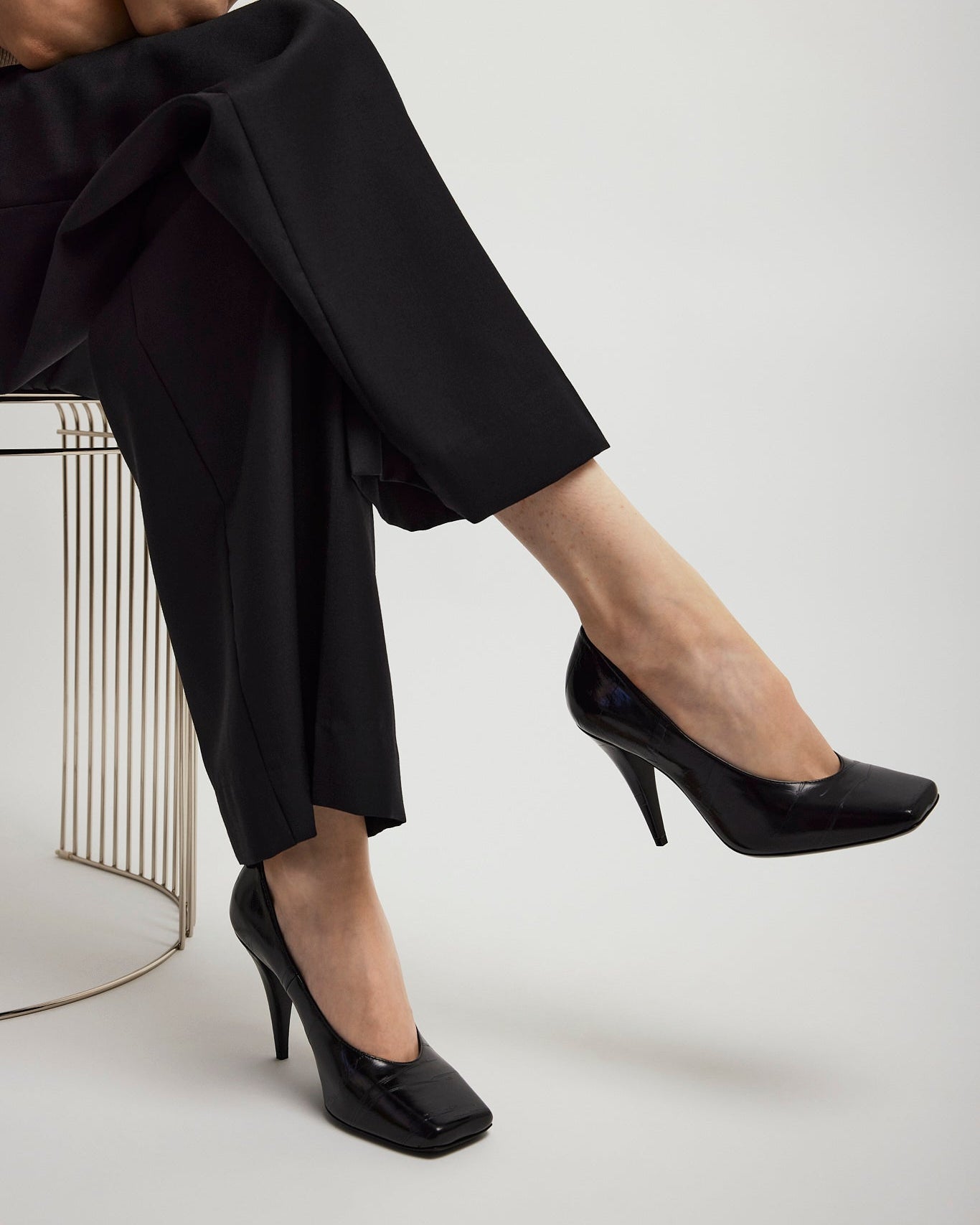 Person wearing black high-heeled shoes and pants on a white background