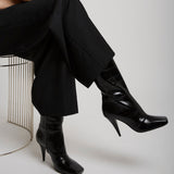 Person wearing black high-heeled shoes and black pants sitting on a chair.