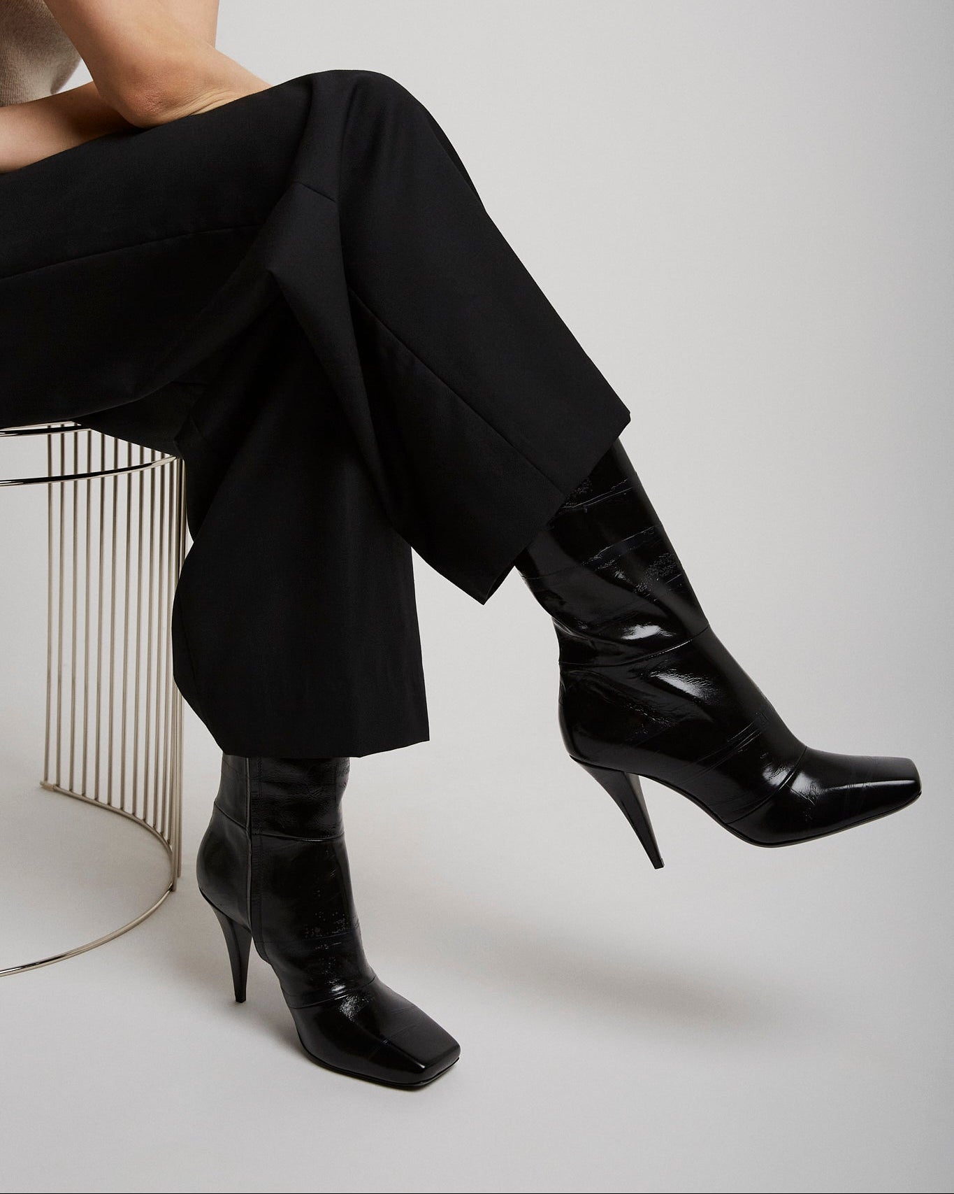 Person wearing black high-heeled shoes and black pants sitting on a chair.