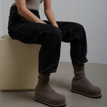 Person wearing brown knit boots sitting on a white block against a plain background