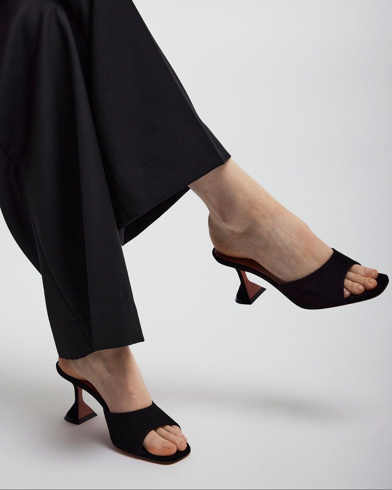 Person wearing black high-heeled shoes and black pants on a white background