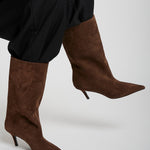 Brown knee-high boots worn with black pants on a light gray background