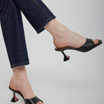 Black high-heeled shoes worn with blue jeans on a light gray background