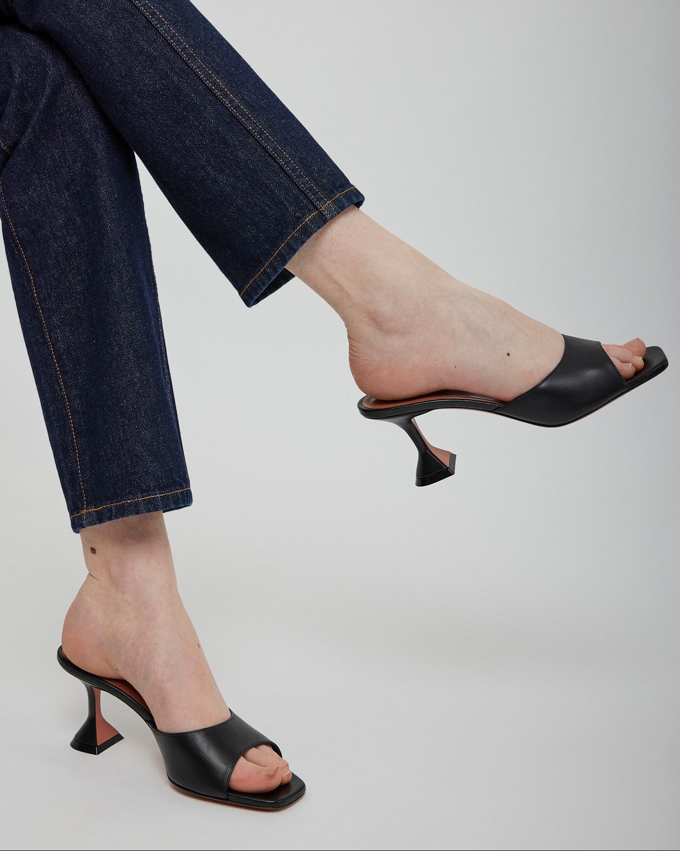 Black high-heeled shoes worn with blue jeans on a light gray background
