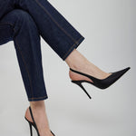Black high-heeled shoes worn with blue jeans on a light gray background