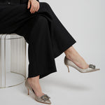 Person wearing black outfit and beige high-heeled shoes with decorative embellishments on a white background
