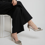 Person wearing black outfit and beige high-heeled shoes with decorative embellishments on a white background