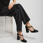Person wearing black shoes sitting on a metal stool against a white background