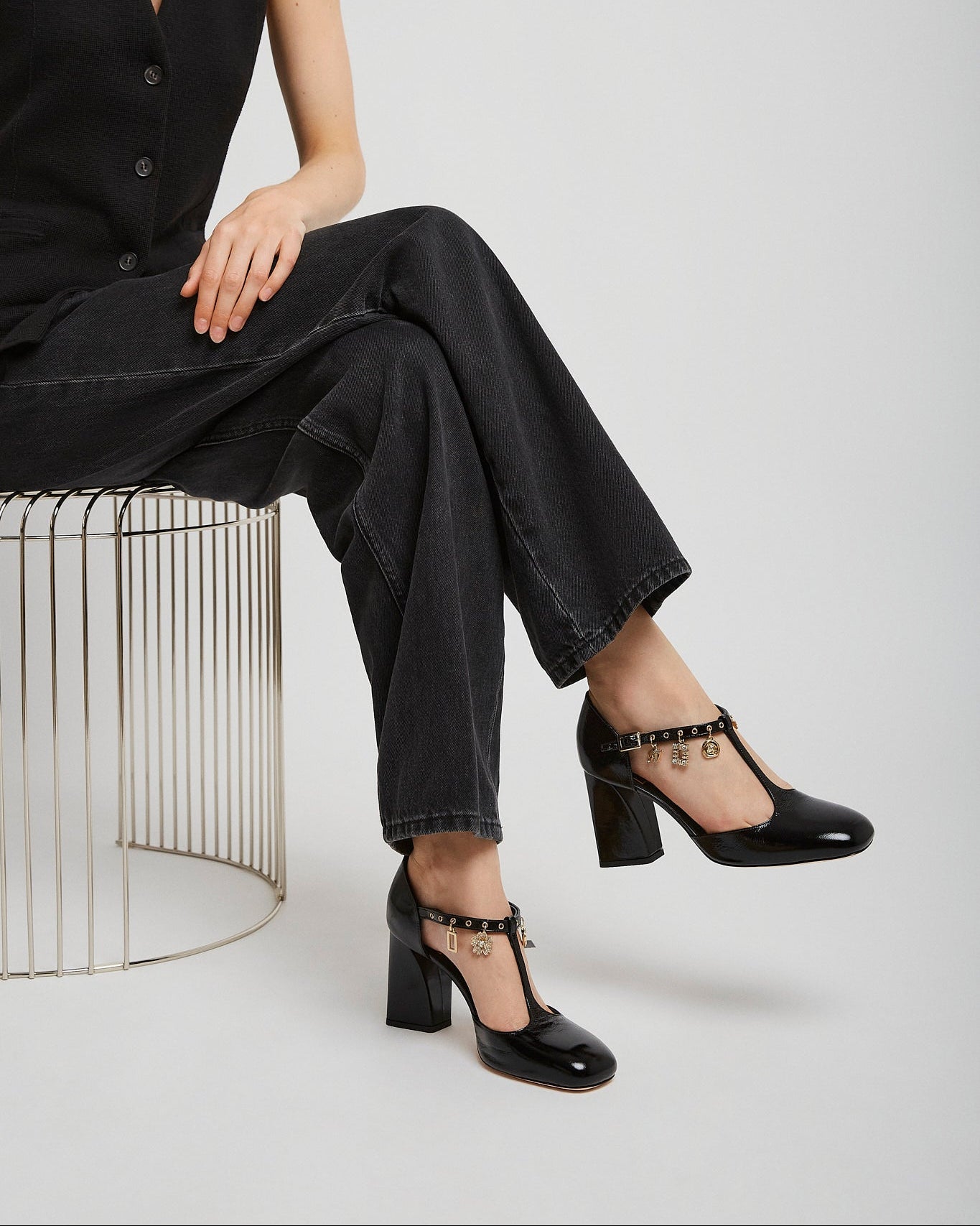 Person wearing black shoes sitting on a metal stool against a white background