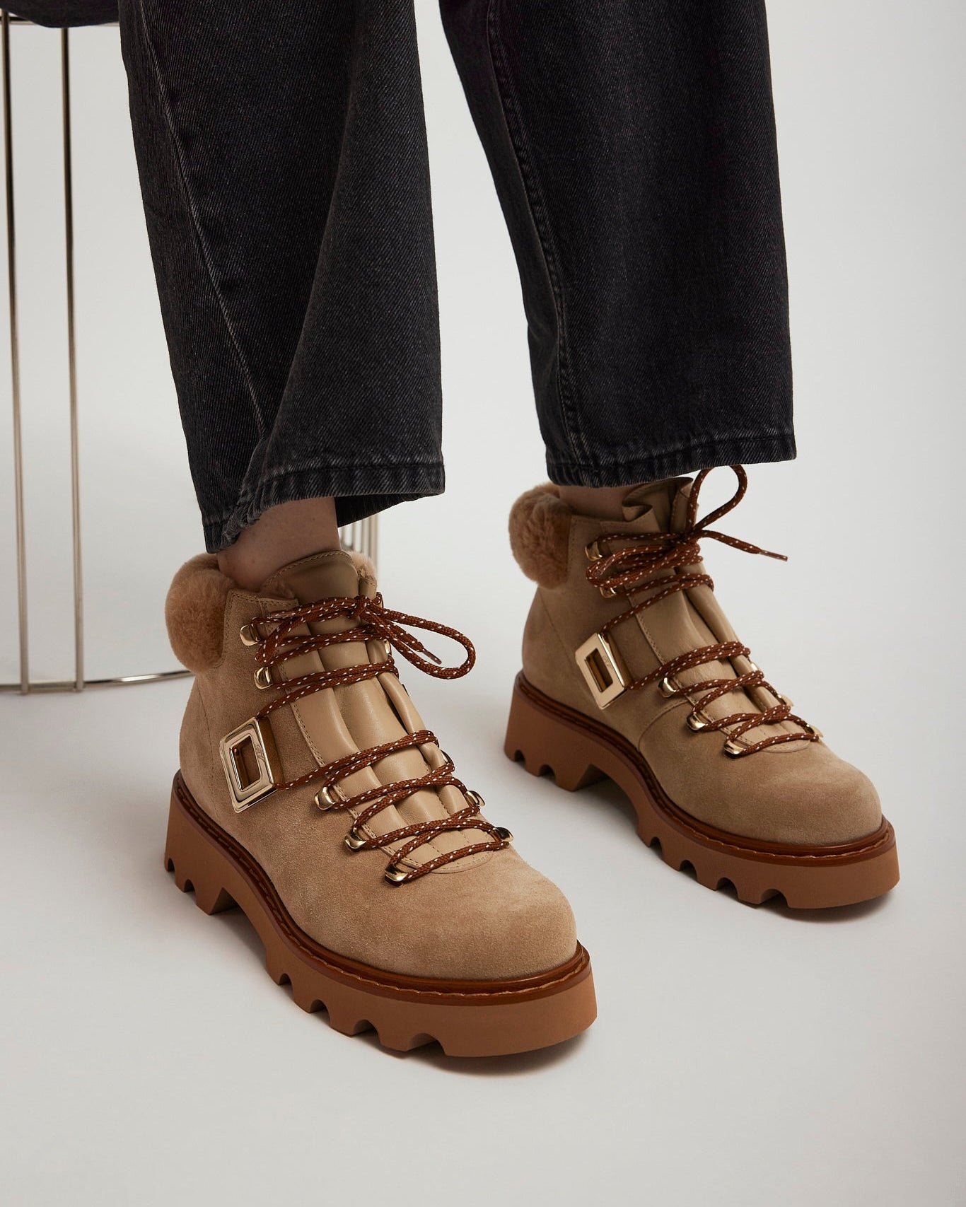 Tan hiking boots with fur trim worn with dark jeans on a light background
