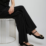 Person wearing a black outfit with wide-leg pants and black shoes on a white background