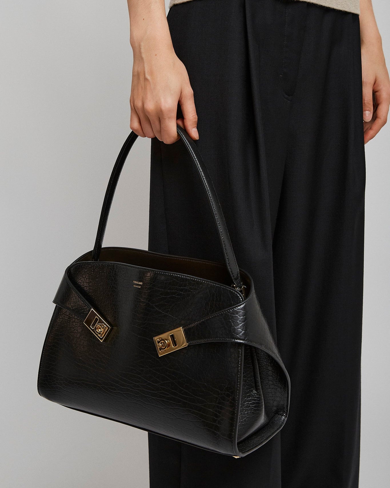 Person holding a black handbag with gold accents on a plain background