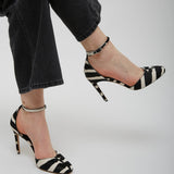 Black and white striped high-heeled shoes worn with black pants on a light gray background