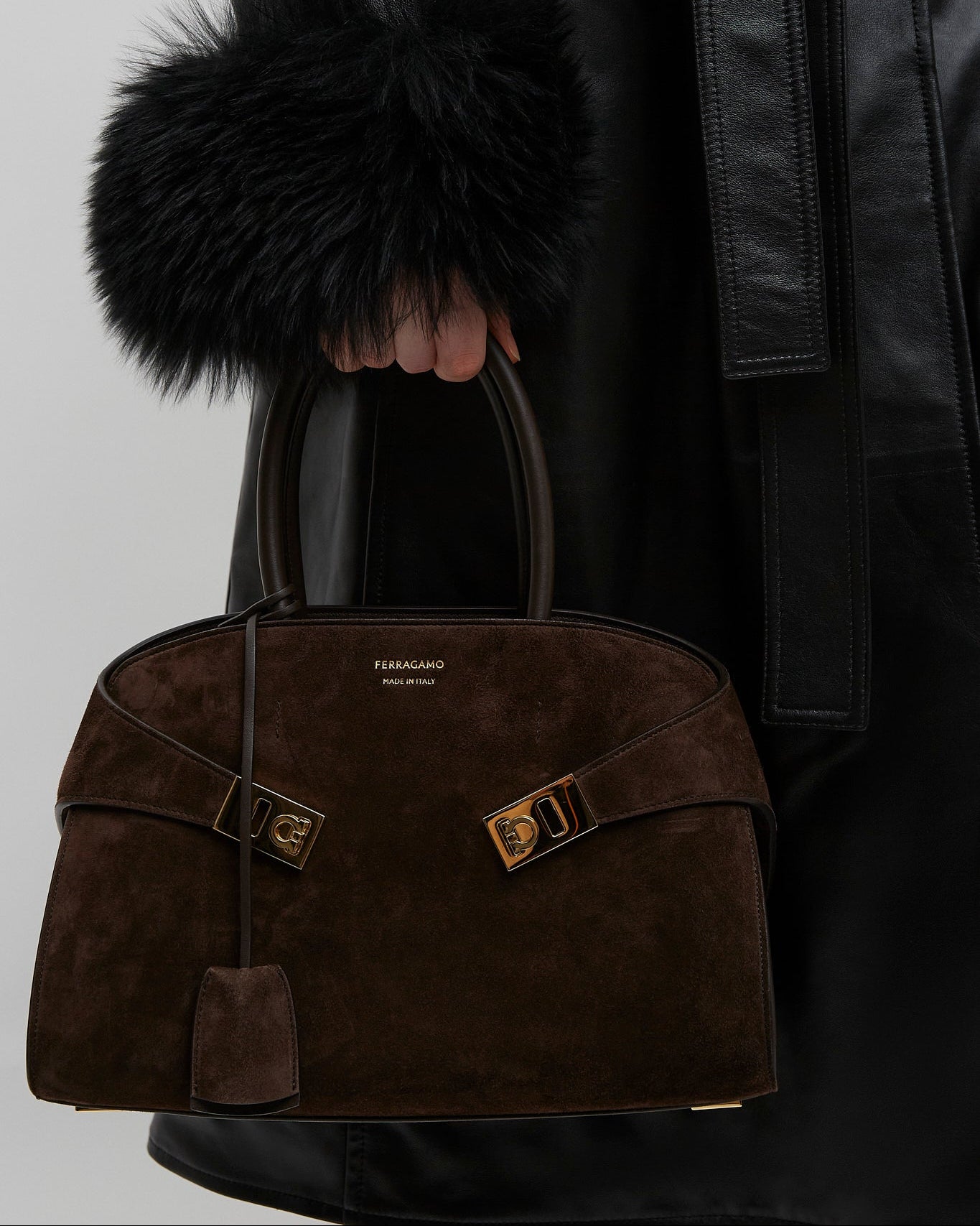 Brown textured handbag with gold accents held by a person wearing a black coat.