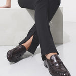 Person wearing black pants and brown shoes sitting on a white surface.