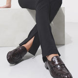 Person wearing black pants and brown shoes sitting on a white surface.