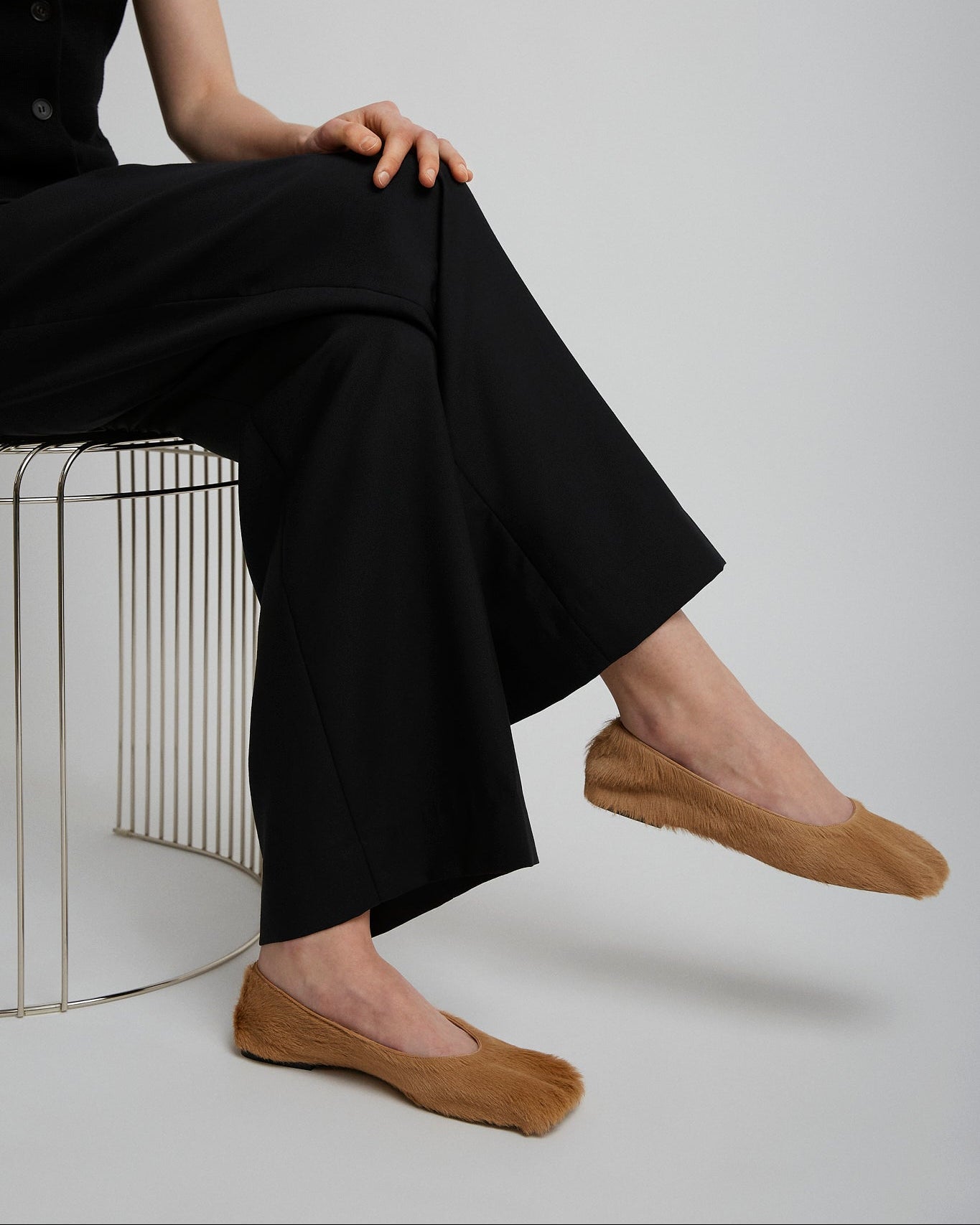 Person wearing black pants and brown shoes sitting on a white surface.