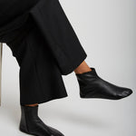 Person wearing black leather ankle boots and pants on a white background
