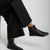 Person wearing black leather ankle boots and pants on a white background